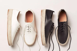 Bespoke handmade shoes in white and black leather lace-up espadrilles with woven soles on a light background.