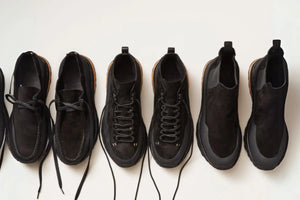 Eco-friendly leather shoes displayed in a row featuring various black suede and leather sneaker designs with natural soles.