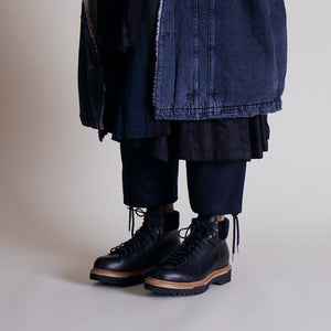 Black leather utility boots with rugged soles styled under layered navy and denim garments.