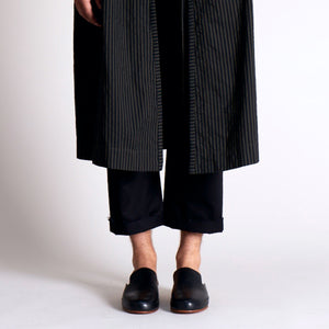 Black leather mules paired with rolled-up black trousers and a striped overcoat.