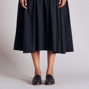 Handmade black leather mules worn with a black midi skirt in a studio setting.