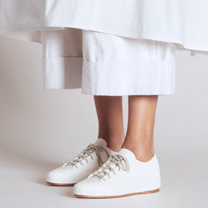 Handmade all white leather sneakers paired with a layered white outfit in a studio setting.