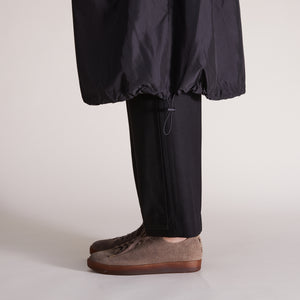 Grey suede sneakers with brown soles styled with black pants and a cinched black jacket.