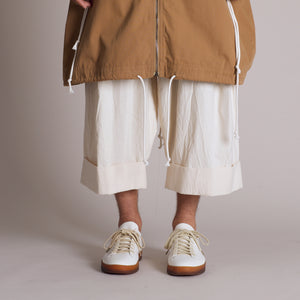 White sneakers with brown rubber sole worn with cuffed cream trousers and a casual jacket.