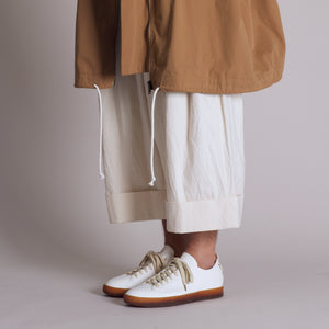 Handmade white sneakers with brown sole paired with wide cropped pants and a tan jacket.