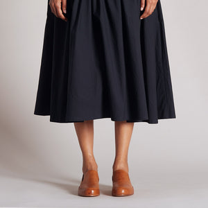 Brown leather mule shoes paired with a black midi skirt in a clean background.