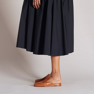 Tan leather mules worn with a flowing black skirt in a side view profile.